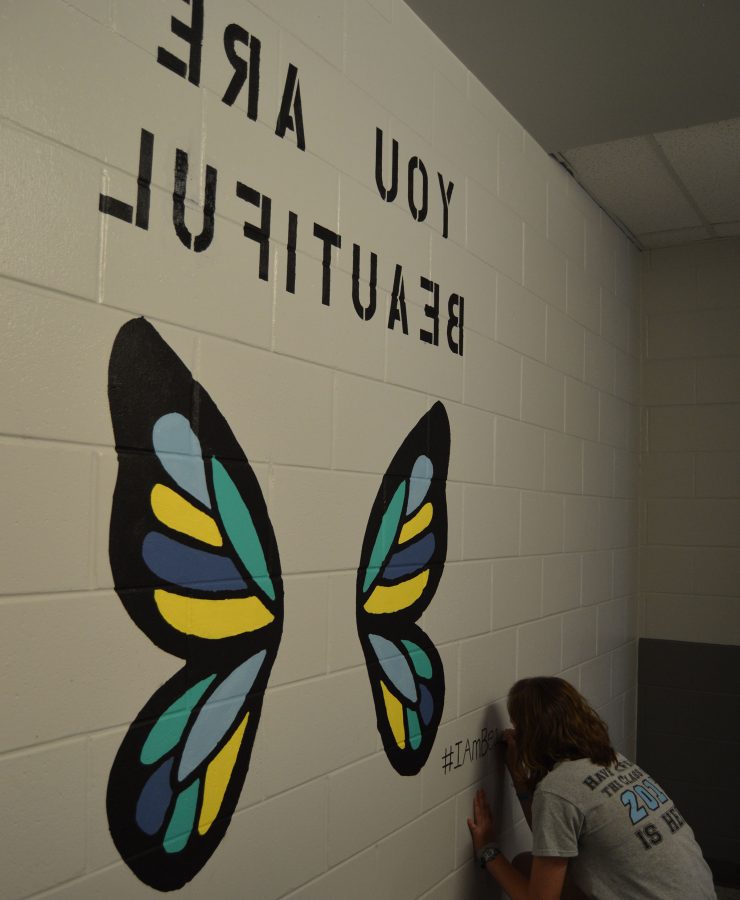 Senior Lizzie Marvin writes “#IAmBeautiful” in the corner of her butterfly wing mural in the upper house girls’ bathrooms.  Marvin intended for girls who take selfies with the murals to post them using the hashtag so she could see what people thought of her project.