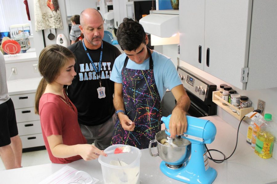 Culinary teacher Matthew Thompson supervises while juniors Samantha Gilman and Grant Dettman mix ingredients for cookie dough. Because of an increase in students signing up for the class, three teachers will teach culinary next year.