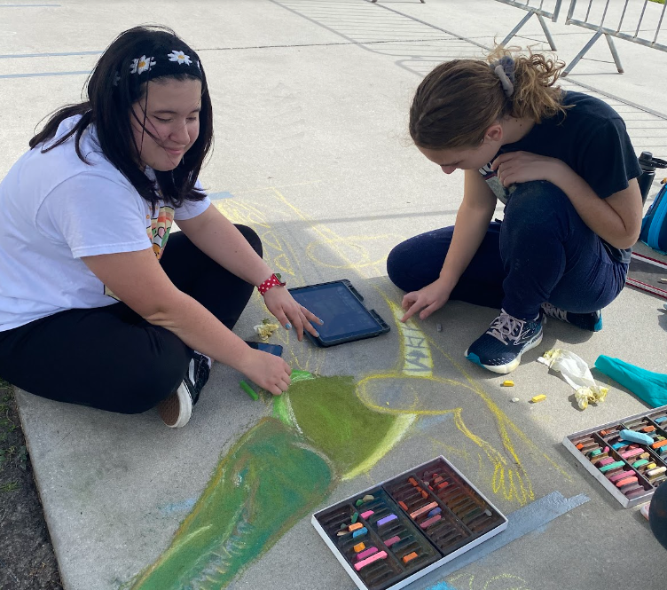 Juniors Anna Lawrence and Abby Stevenson draw an alligator in chalk at the Creative Arts Festival mural competition. The contest is the second one that the club has participated in this year, following the Arts for Life festival. 