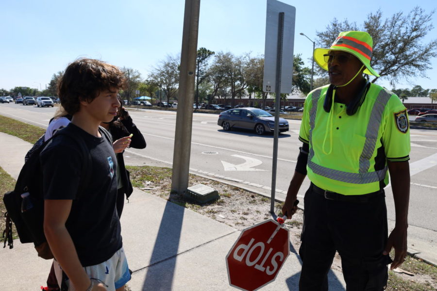 Crossing guard Larry Miller chats with students after school while helping them cross Lockwood Boulevard. Miller gets to know all the students he serves, developing personal relationships through positive daily conversations.