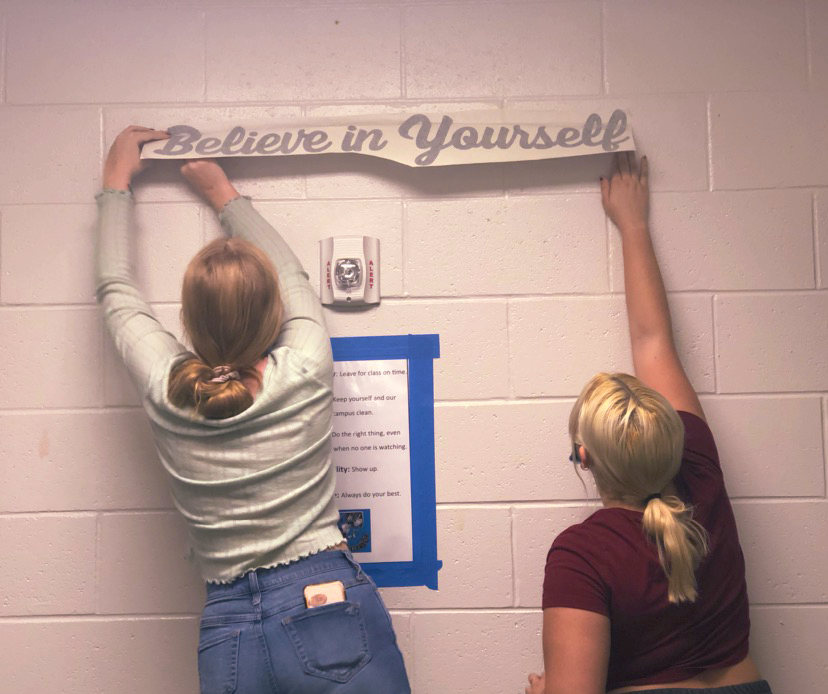Freshmen+Margaret+Neely+and+Katie+Pollack+are+student+volunteers+on+the+committee.+They+hang+up+vinyl+signs+with+positive+affirmations.