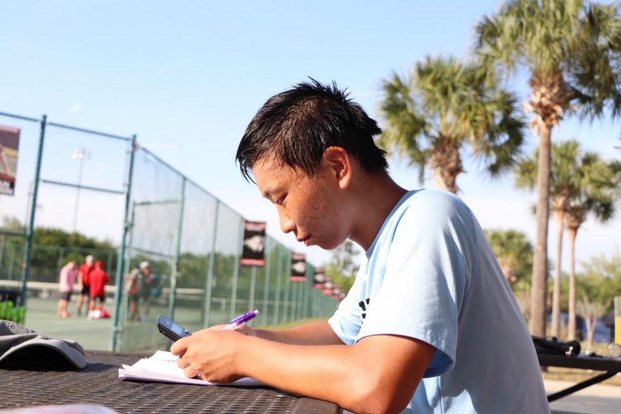 Senior Nicolas Cai works on his homework at tennis practice. Being in the gifted program often required setting aside a lot of time for assignments.