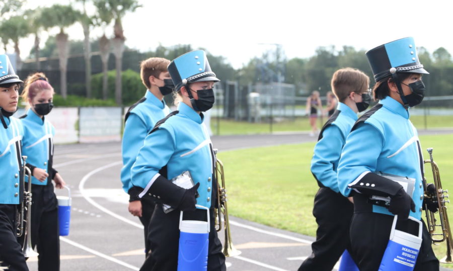 Sophomore Sophia Garbelman walks with the band to the stands before the game. The band walked together to the stands in uniform, including matching masks and water bottles.