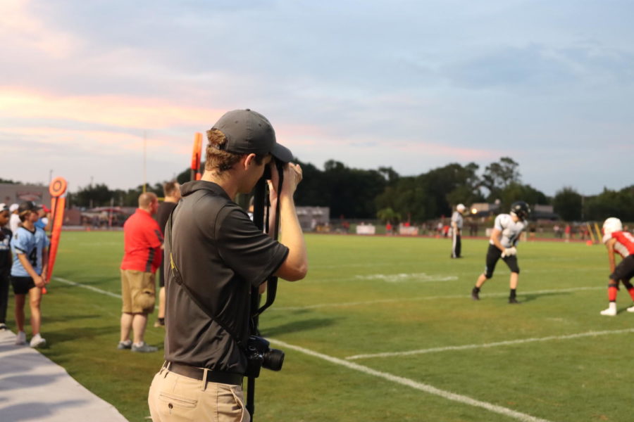 James Hilston standing on the sideline and taking photos of varsity football pictures of wide receiver Caleb Barber. Hilston attends every football game and takes pictures for the program.