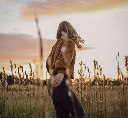 One of Karlie Marinis photo ambassadors poses in a field and looking at the sunset. She gets to post these photos for free on her own Instagram.