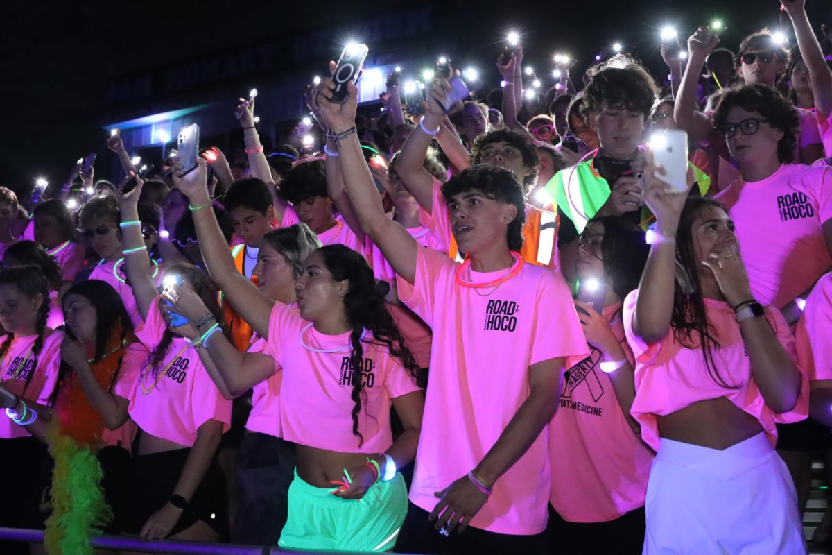 Seniors show their school spirit in their pink neon homecoming shirts. They shine their flashlights, lightning up the whole stadium. 