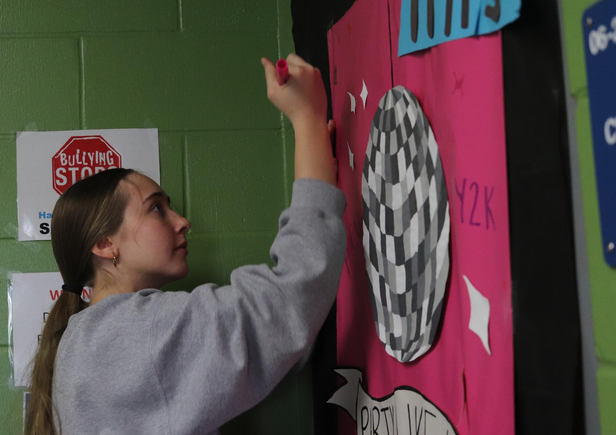 Junior Kiera McDermott decorates math teacher Lois Arp's door in building six. Leadership hosted a door and hallway decorating contest where groups came in on the Sunday before homecoming week to get the school ready.