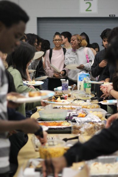 Students select food arranged on the cafeteria table. The clubs organized their different foods and students stood with their plates in a line moving to grab the food they please. 