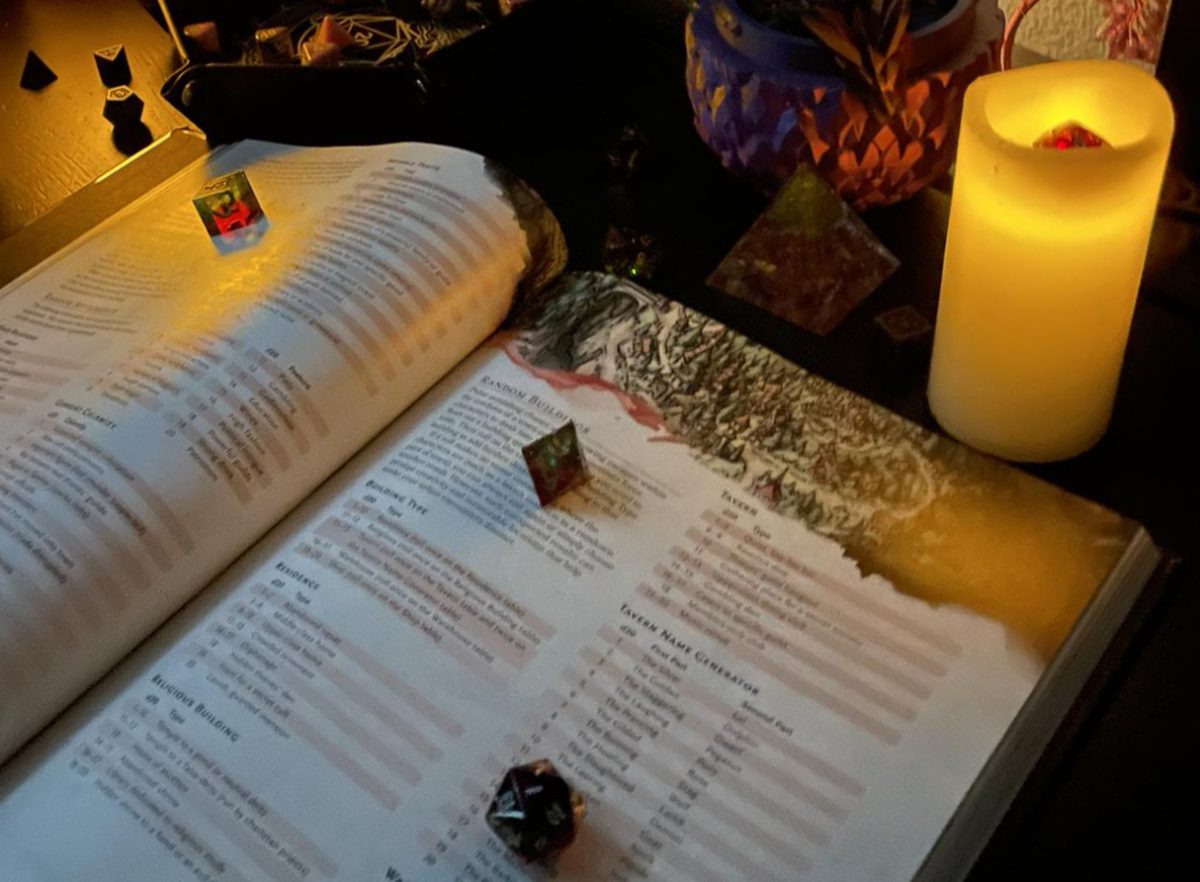 A player's handbook sits beneath dice surrounded by candles. DMs usually have a physical copy of the handbook on hand during sessions. Photo l Dee Floyd. 