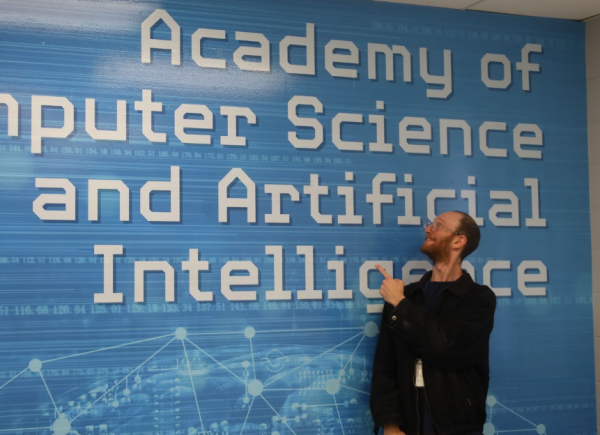 Benjamin Ross stands in front of a wall in his Applications of AI classroom.
