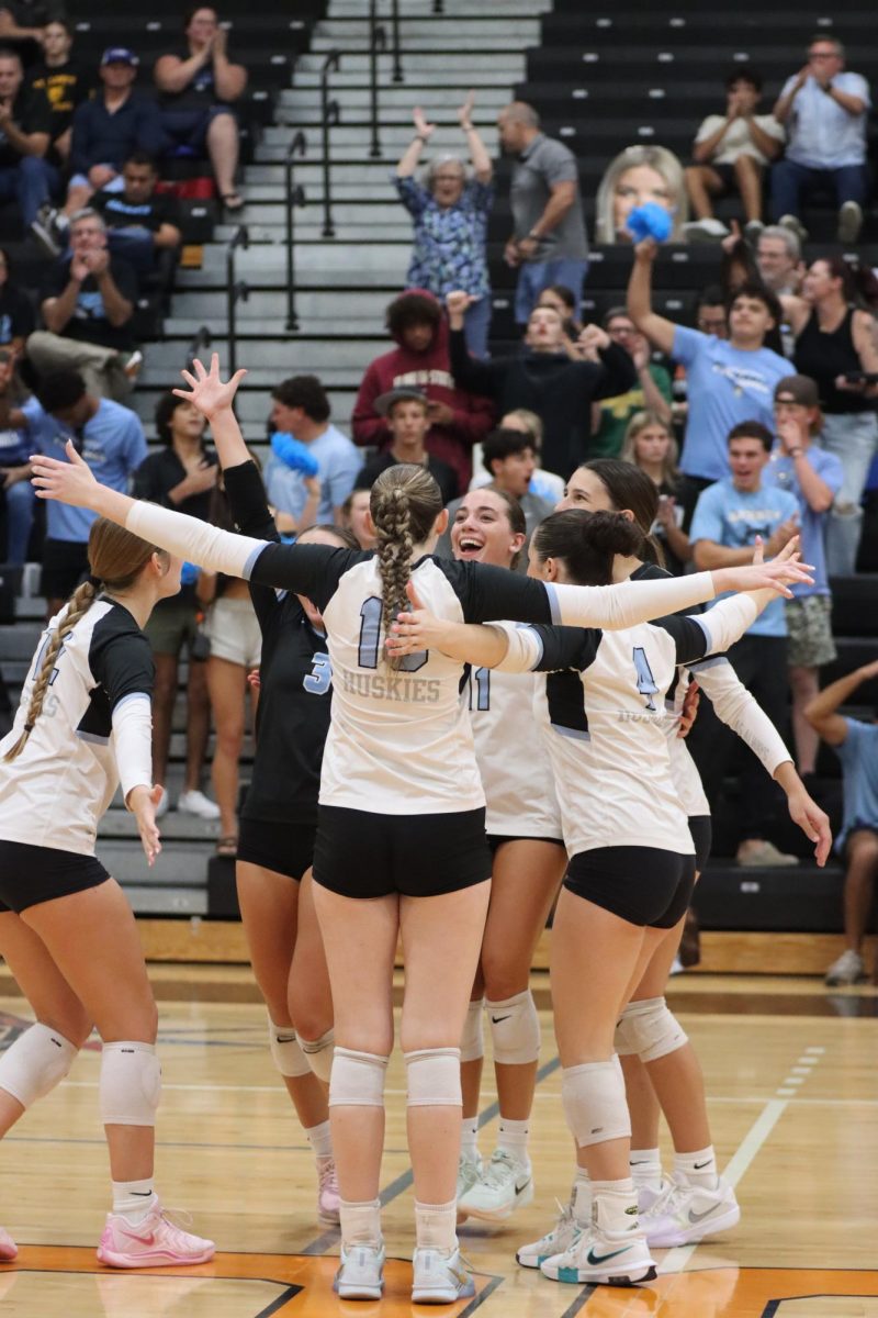 The girls varsity volleyball team cheers during a game at Oviedo, with the student section behind them. The successes of athletic teams including girls volleyball have contributed to a rise in school spirit this year.