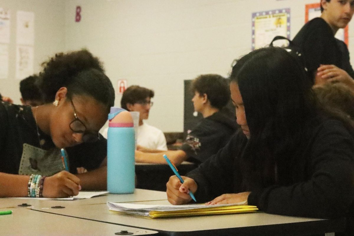 Freshmen Kannika Nelse and Mya Nunes work on paper assignments in English class. When educational servers experience technical difficulties, alternative lesson plans are often implemented.