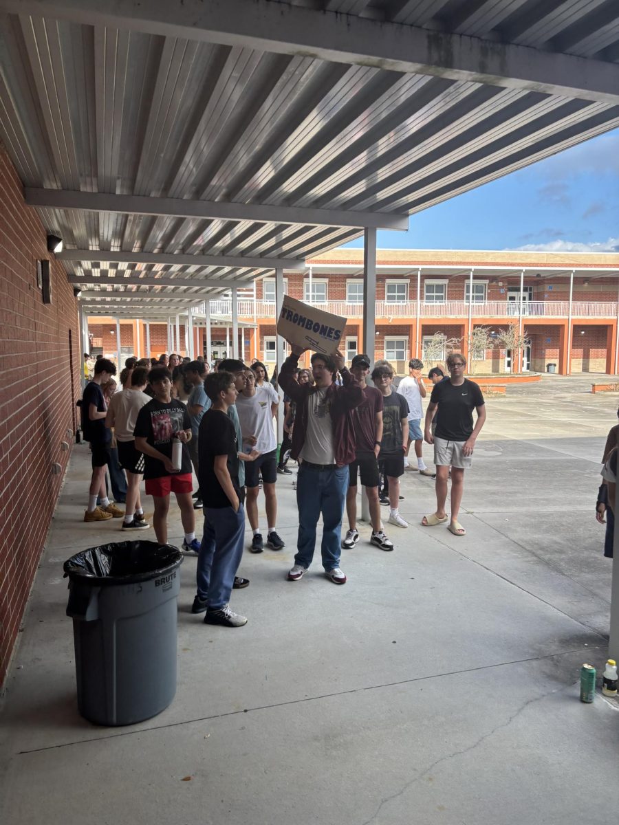 Sophomore John Watson holds up the trombone sign to gather up his section. With the chaos of incoming and current members, it is hard to keep everyone together. Photo by Caityln Shaffer